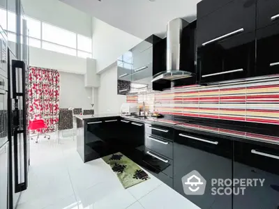 Modern kitchen with sleek black cabinets and colorful backsplash in a bright open layout.