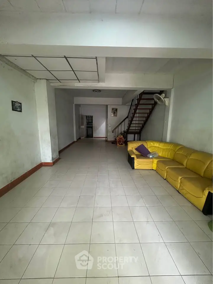 Spacious living room with yellow sofa and staircase in minimalist home interior.
