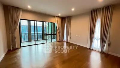 Spacious empty room with hardwood floors and large windows leading to a balcony.
