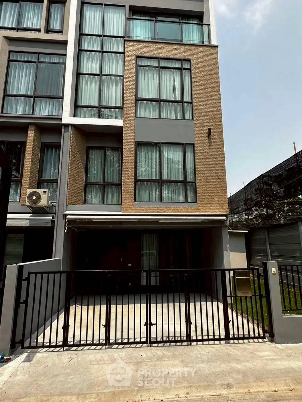 Modern multi-story townhouse with large windows and gated entrance in urban setting.