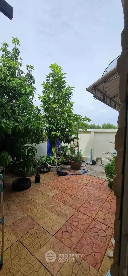 Charming garden patio with lush greenery and tiled flooring, perfect for outdoor relaxation.