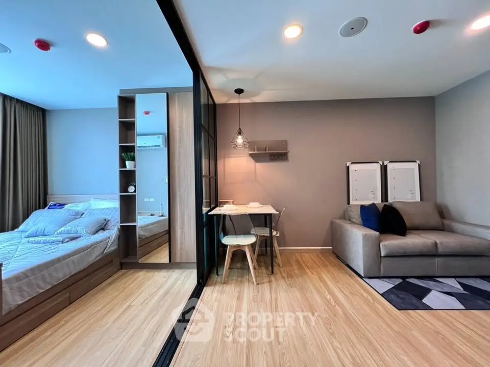 Modern studio apartment with cozy living area and stylish bedroom separated by glass partition.