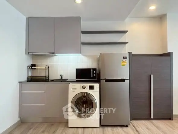 Modern kitchen with sleek cabinets, washing machine, and stainless steel fridge.