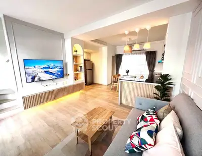 Modern open-plan living room with stylish decor and kitchen area, featuring a wall-mounted TV and cozy seating.