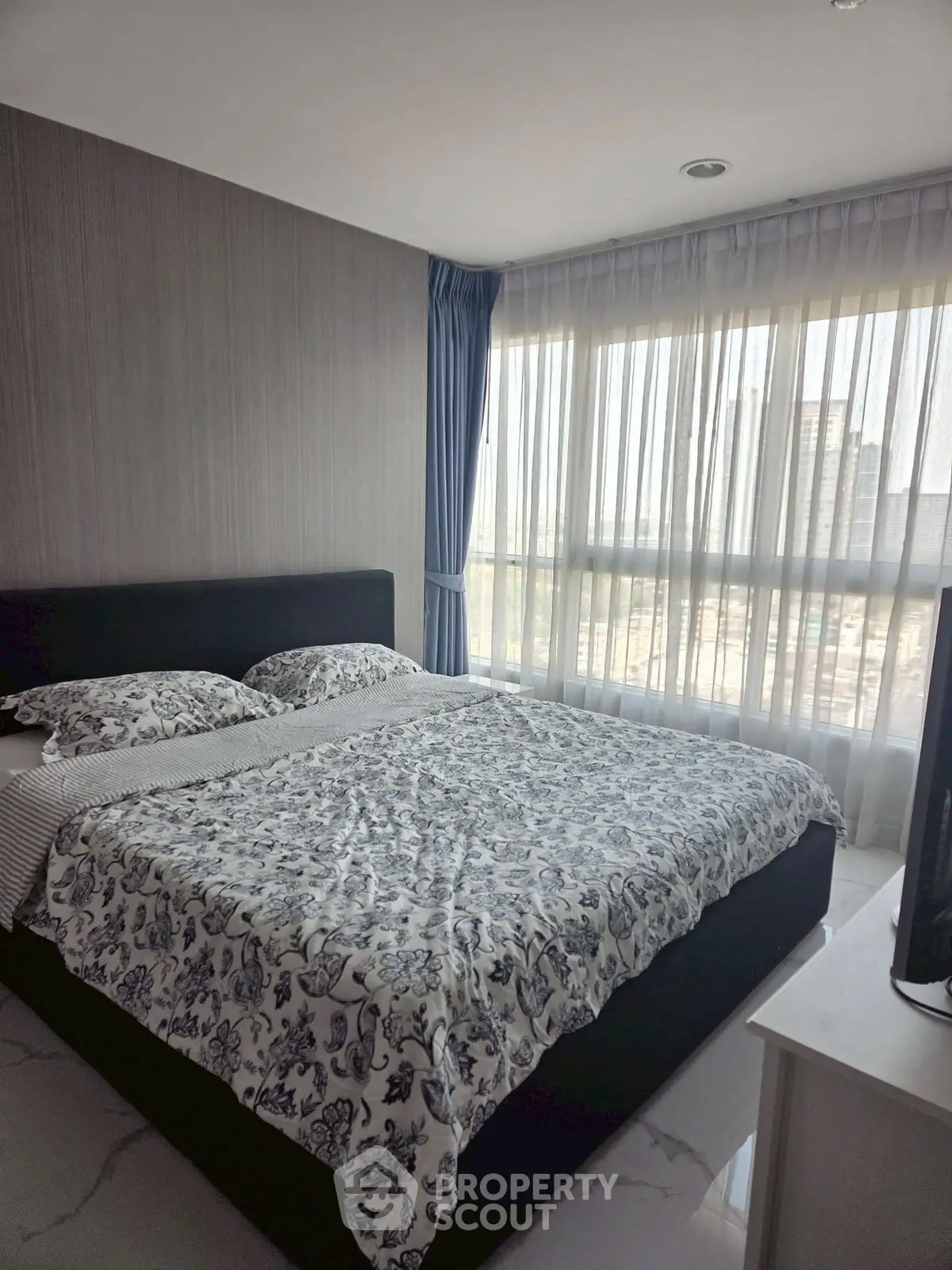 Modern bedroom with large window and stylish decor in urban apartment.