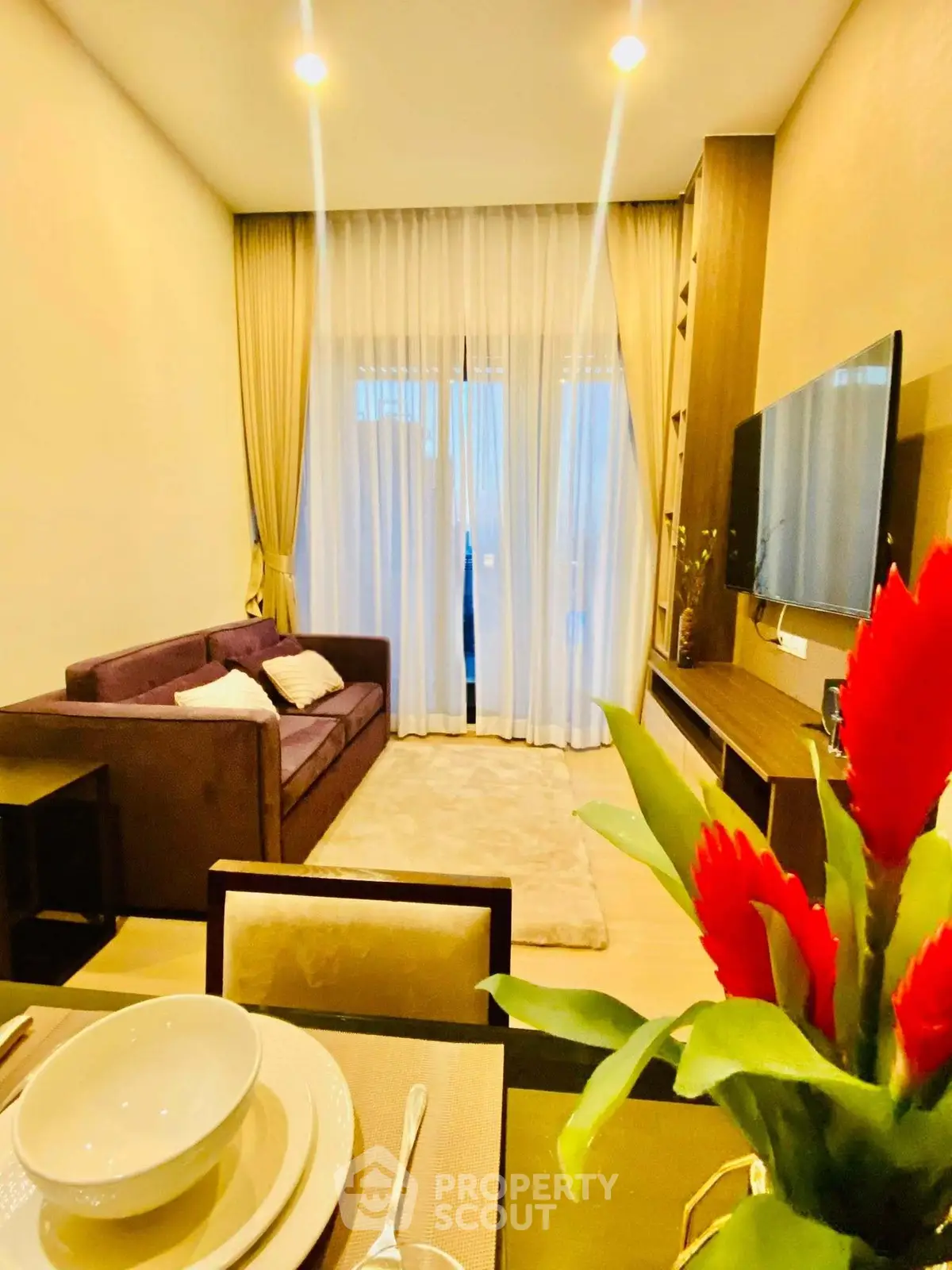 Modern living room with elegant decor and large window, featuring a cozy sofa and wall-mounted TV.
