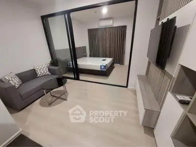 Modern apartment with sleek living room and bedroom separated by glass wall, featuring stylish decor.