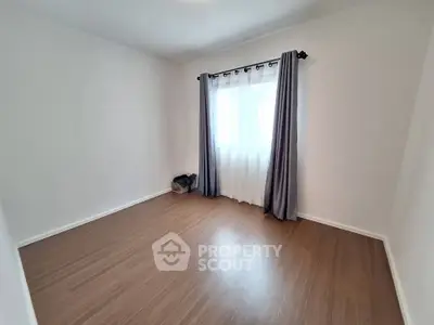 Spacious empty room with wooden flooring and large window with curtains, perfect for customization.