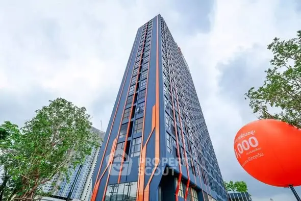 Modern high-rise building with unique architectural design and vibrant colors, surrounded by lush greenery.