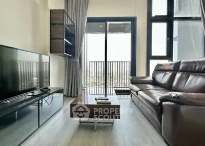 Modern living room with leather sofa and large TV, featuring floor-to-ceiling windows and balcony access.