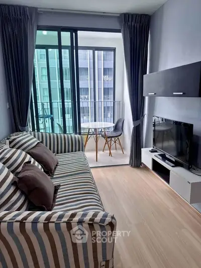 Modern living room with striped sofa and TV, leading to a balcony with city view.
