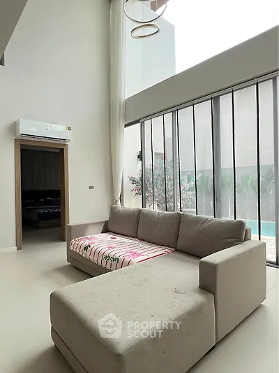Spacious living room with large windows and modern sofa overlooking a pool area.