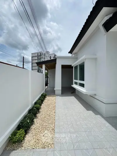 Modern white exterior of a single-story home with a neat gravel pathway and lush greenery.