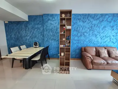 Modern living room with blue accent wall, sleek dining area, and cozy brown leather sofa.