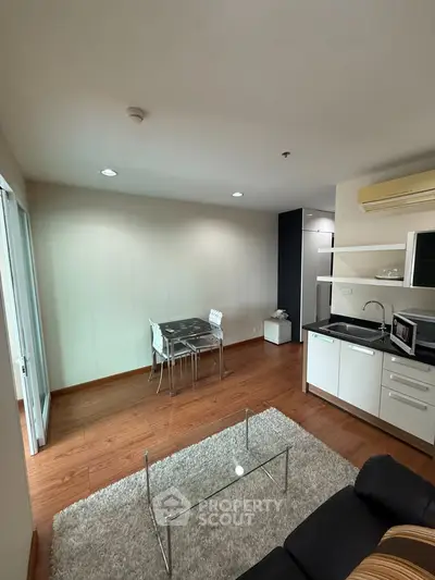 Modern living room with open kitchen, wooden flooring, and stylish furniture in a cozy apartment.