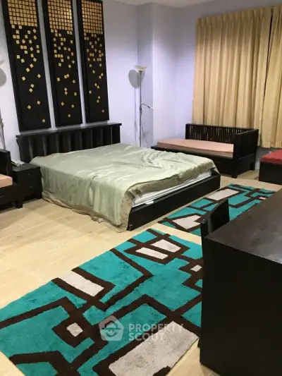 Spacious bedroom with modern decor and stylish furniture, featuring a cozy bed and vibrant rug.