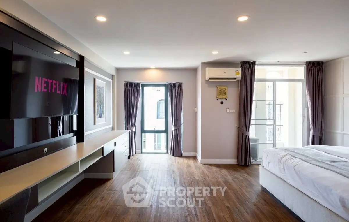 Spacious modern bedroom with wooden flooring and large TV, perfect for relaxation.