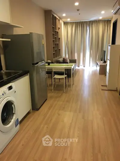 Modern open-plan living room with kitchen, featuring wooden flooring and natural light.