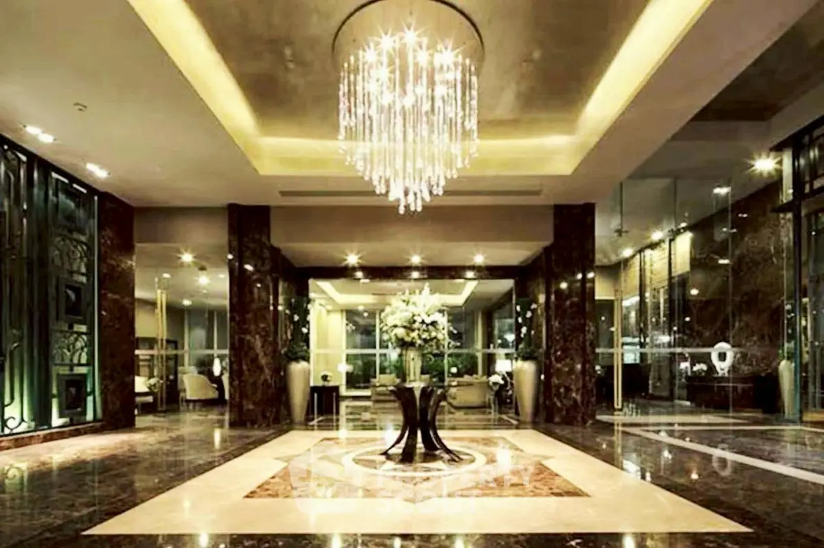Luxurious building entrance with elegant chandelier and marble flooring, exuding sophistication and grandeur.