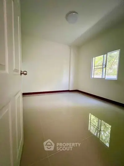 Spacious empty room with glossy tiled floor and natural light from window.