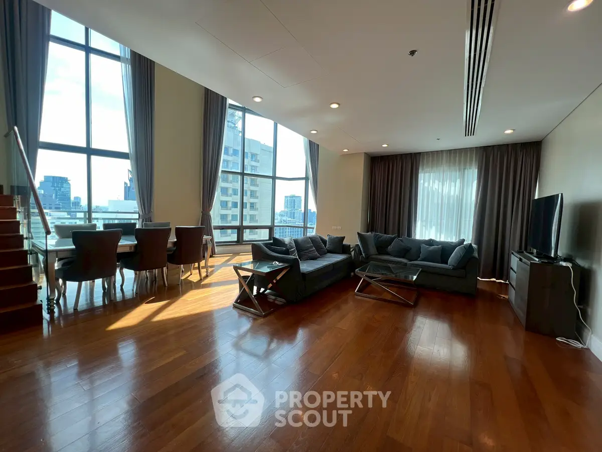 Spacious modern living room with large windows and city view, featuring elegant furniture and wooden flooring.