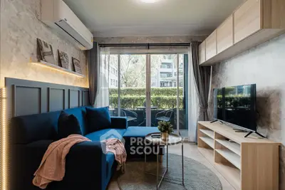 Modern living room with stylish decor and large window overlooking greenery, featuring a cozy blue sofa and sleek TV setup.