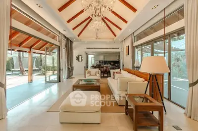 Luxurious open-plan living room with high ceilings and elegant decor, featuring large windows and a stunning chandelier.