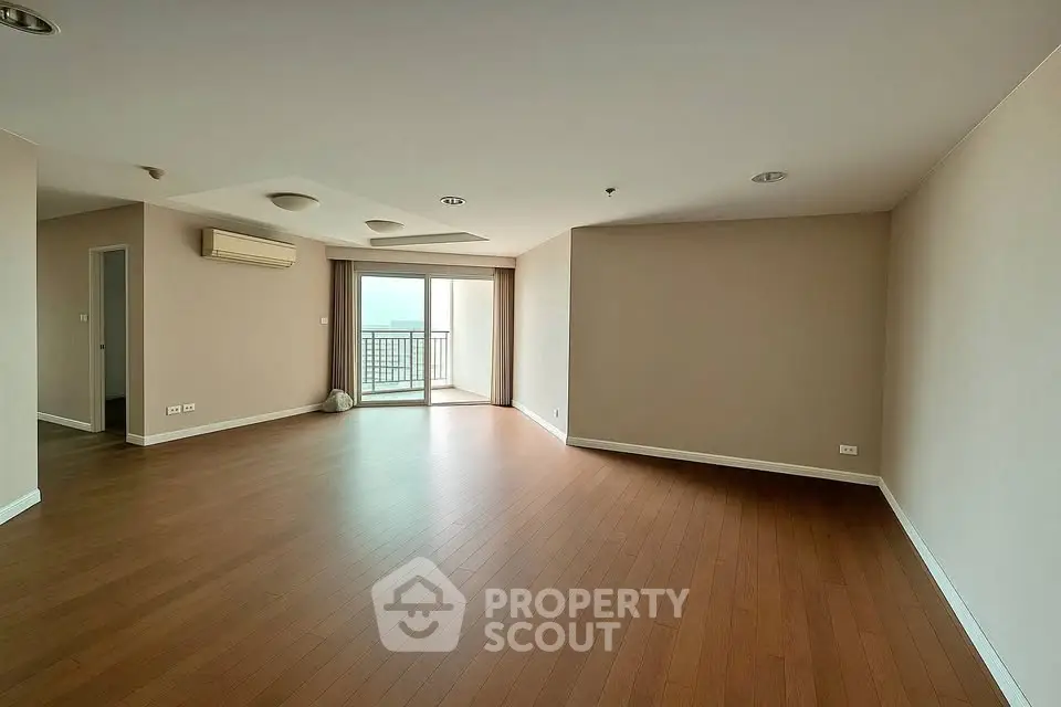 Spacious empty living room with wooden flooring and balcony access.