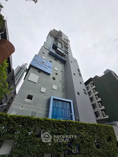 Modern high-rise building with sleek architecture and lush greenery in urban setting.