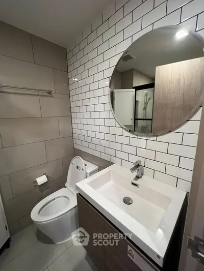 Modern bathroom with sleek fixtures and stylish tile design, featuring a round mirror and contemporary vanity.