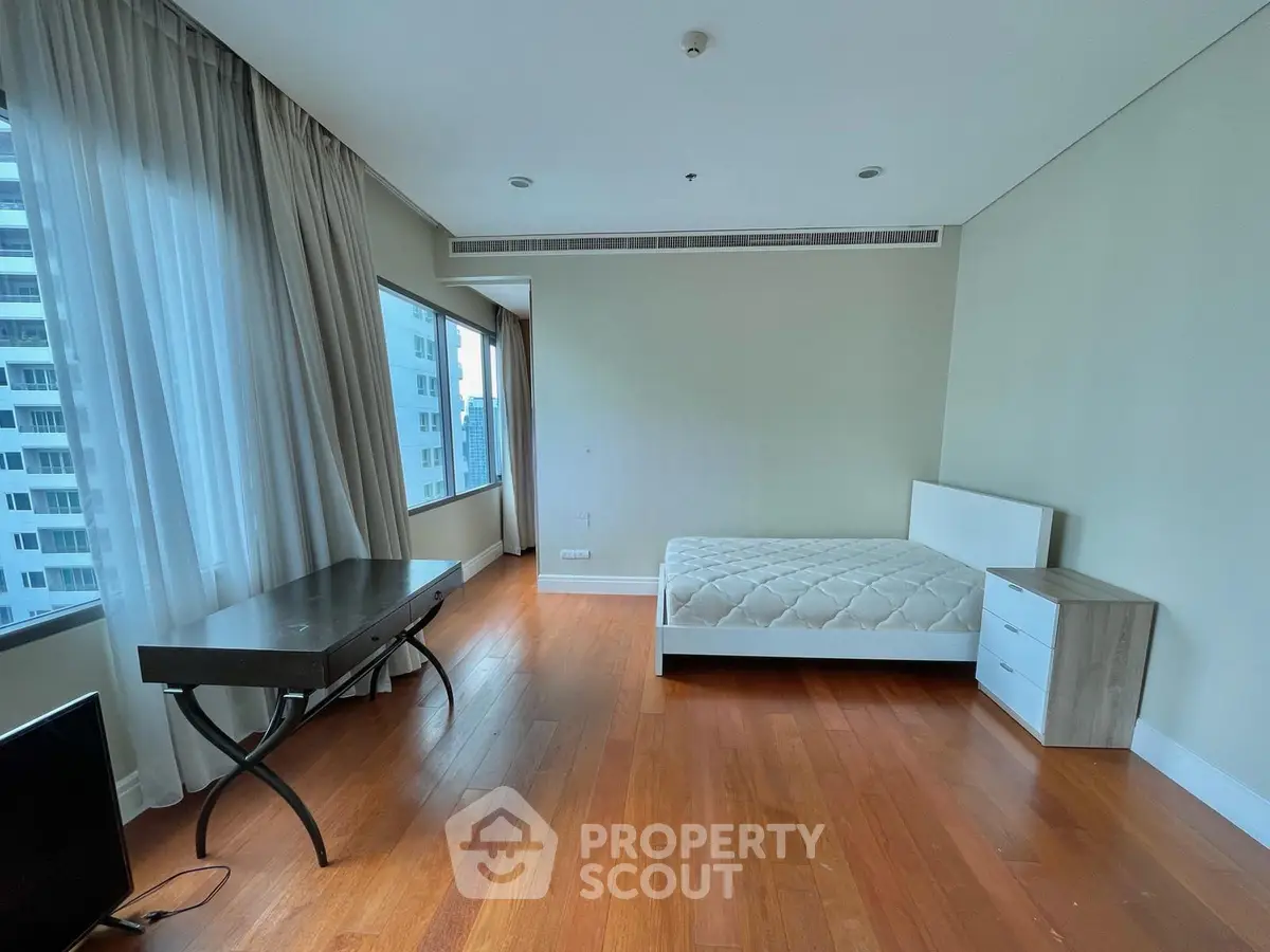 Spacious bedroom with large windows and wooden flooring in modern apartment.