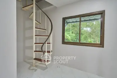 Modern spiral staircase in a bright room with large window and garden view.