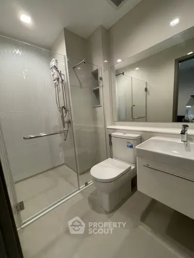 Modern bathroom with glass shower enclosure, sleek white fixtures, and large mirror creating a spacious feel in a well-lit, clean interior.