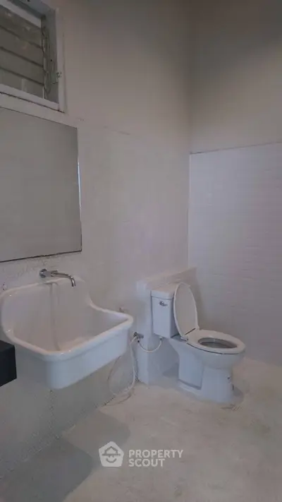 Minimalist bathroom with white fixtures and tiled walls, featuring a sink and toilet.