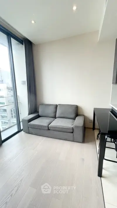 Modern living room with sleek gray sofa and large windows offering city views.