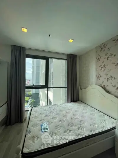 Bright bedroom with large window and floral wallpaper, featuring a comfortable bed and modern decor.