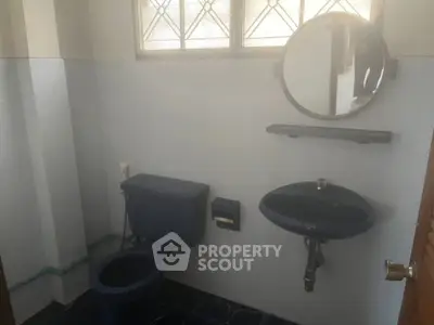 Compact bathroom with classic blue fixtures, wall-mounted sink, and a large mirror, set against a light blue wall and dark floor tiles.