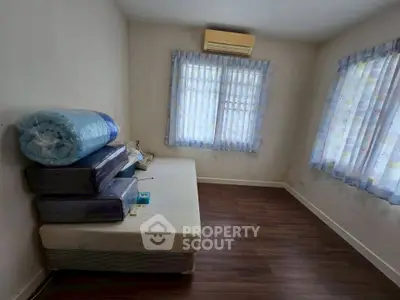 Spacious bedroom with wooden flooring and natural light, featuring air conditioning and simple decor.