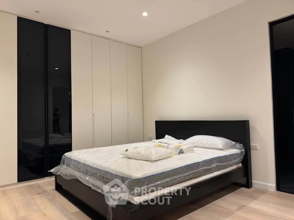 Modern bedroom with sleek black bed frame and spacious wardrobe in a stylish apartment.