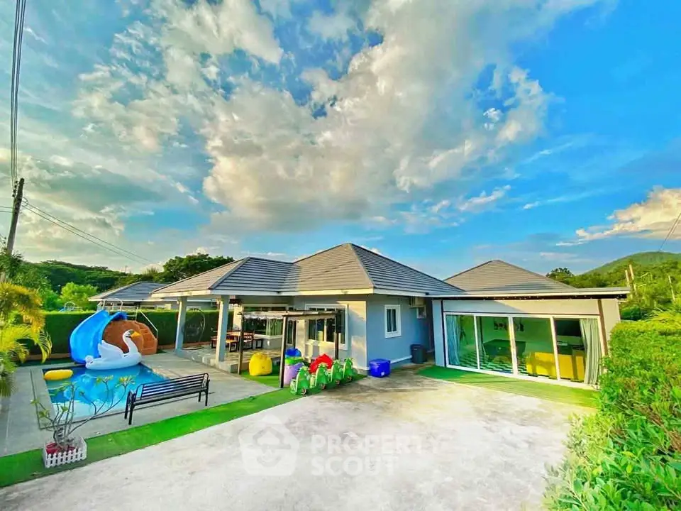 Stunning modern home with spacious yard and vibrant outdoor play area under a clear blue sky.