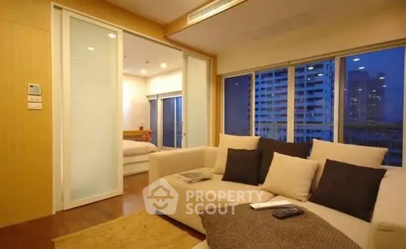 Modern living room with cozy sofa and city view, featuring sliding doors to bedroom.