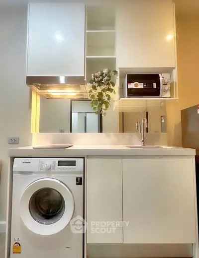 Modern compact kitchen with washing machine and microwave, sleek cabinetry, and elegant lighting.