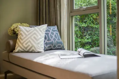 Elegant living room with stylish chaise lounge and large window overlooking lush greenery.