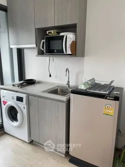 Modern compact kitchen with washing machine and microwave in sleek apartment.
