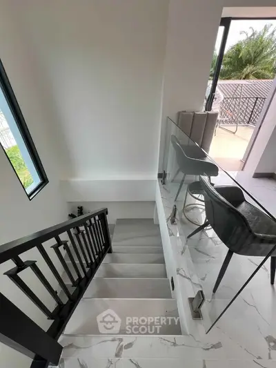 Modern staircase with glass railing leading to a bright balcony with outdoor seating.