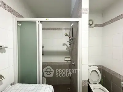 Modern bathroom with shower and toilet in a tiled interior, featuring a sleek design and functional layout.