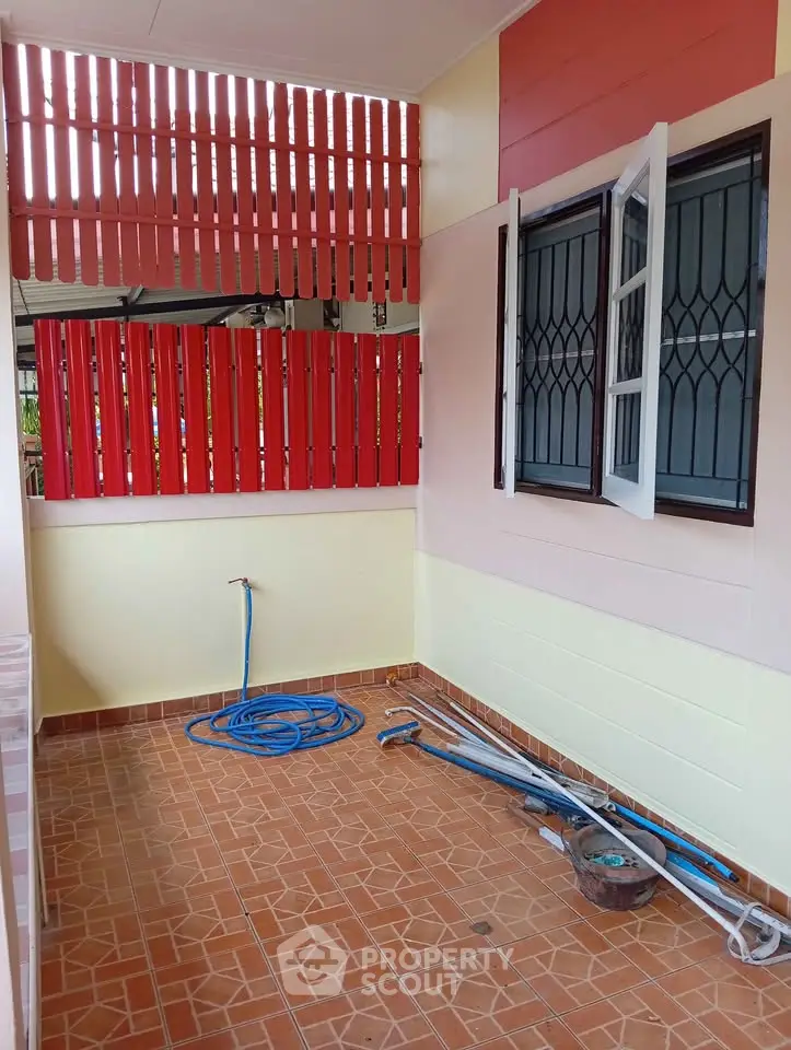 Charming outdoor patio with tiled flooring and vibrant red accents, perfect for relaxation or gardening.