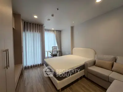 Modern bedroom with cozy bed, sofa, and study area in stylish apartment.