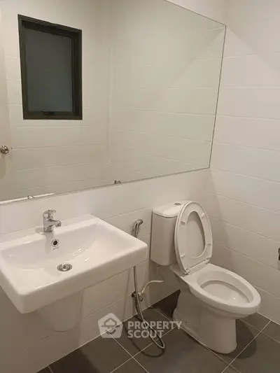 Pristine white bathroom with modern fixtures, including a wall-mounted sink, toilet, and a sleek mirror, offering a clean and minimalistic design.