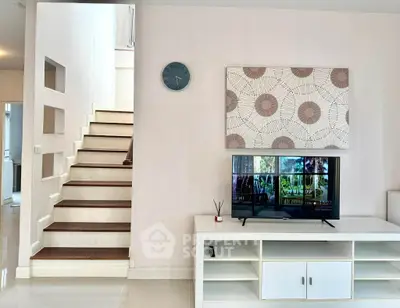 Modern living room with stylish decor and staircase, featuring a TV and elegant wall art.